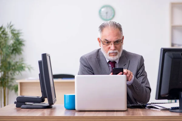 Oude mannelijke baas zit op het bureaublad in het kantoor — Stockfoto