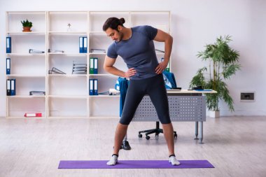 Genç yakışıklı çalışan ofiste spor egzersizleri yapıyor.