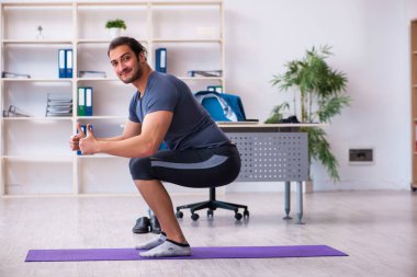 Genç yakışıklı çalışan ofiste spor egzersizleri yapıyor.