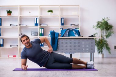 Genç yakışıklı çalışan ofiste spor egzersizleri yapıyor.