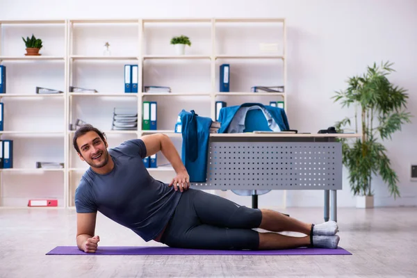 Genç yakışıklı çalışan ofiste spor egzersizleri yapıyor.