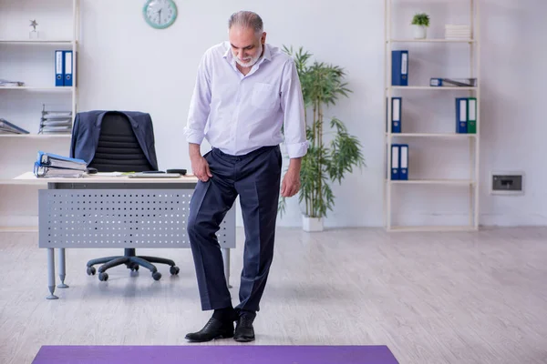 Verouderde mannelijke werknemer doet fysieke oefeningen tijdens de pauze — Stockfoto