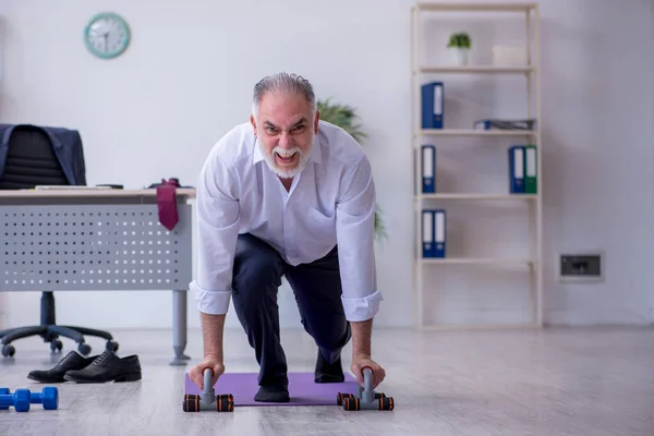 Idősebb férfi alkalmazott, aki a szünetben fizikai gyakorlatokat végez — Stock Fotó