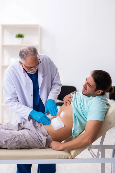 Yaralı genç adam deneyimli erkek doktoru ziyaret ediyor. — Stok fotoğraf