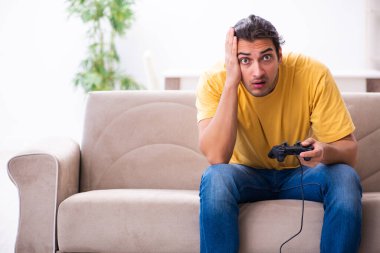Genç adam evde joystick oynuyor.