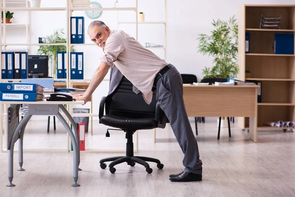 Viejo empleado haciendo ejercicios físicos en el lugar de trabajo —  Fotos de Stock