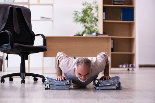 Velho funcionário do sexo masculino fazendo exercícios físicos no local de trabalho — Fotografia de Stock