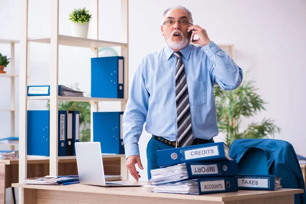 Oude mannelijke boekhouder ongelukkig met buitensporig werk op de werkplek — Stockfoto