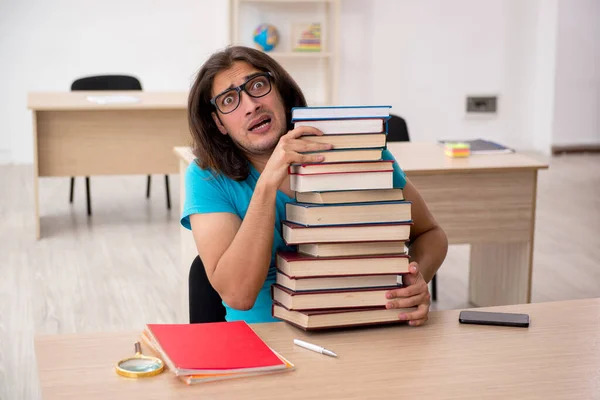 Jonge mannelijke student en veel boeken in de klas — Stockfoto