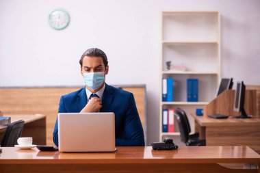 Ofiste maske takan genç bir erkek çalışan.