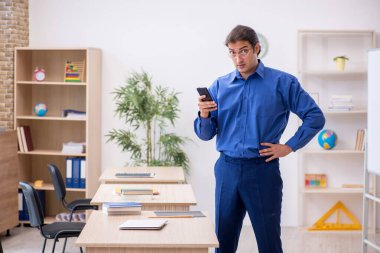 Genç erkek öğretmen ders sırasında elinde akıllı telefon tutuyor.