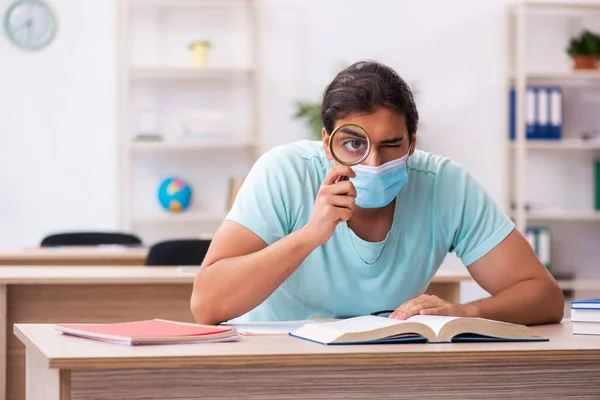 Joven estudiante masculino sentado en el aula usando máscara — Foto de Stock