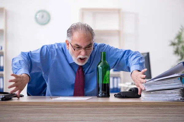 Старий працівник п'є алкоголь в офісі — стокове фото