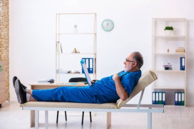 Yaşlı erkek doktor klinikte not alıyor.