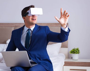 Yatak odasında sanal gerçeklik kulaklığı takan bir iş adamı.