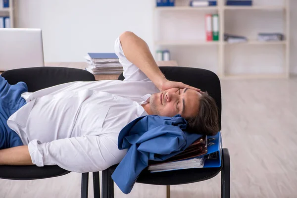 Ung manlig anställd sover på kontoret på stolar — Stockfoto