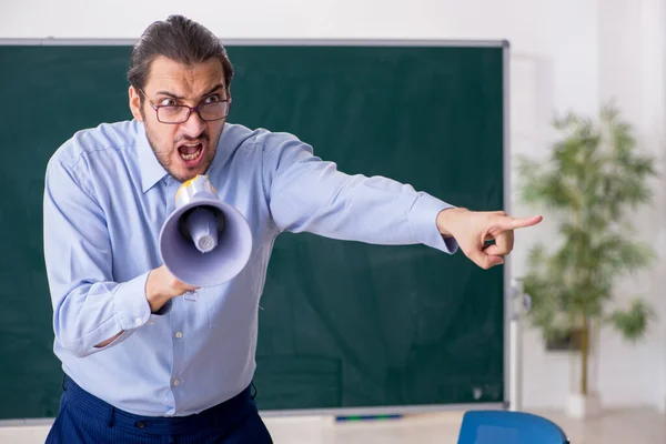 Young male teacher in the classroom holding megaphone — Stock Photo, Image