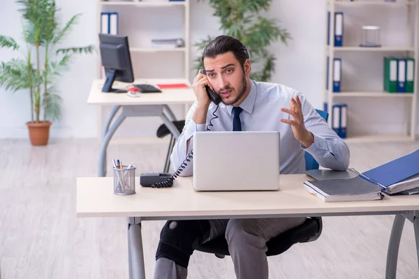 Jeune employé blessé à la jambe qui travaille au bureau — Photo