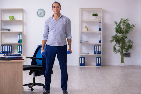 Молодой красивый работник делает упражнения в офисе