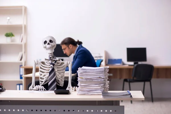 Jeune employé masculin avec des squelettes dans le bureau — Photo