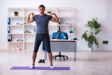 Genç yakışıklı çalışan ofiste spor egzersizleri yapıyor.