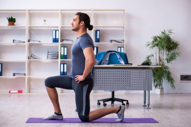 Genç yakışıklı çalışan ofiste spor egzersizleri yapıyor.