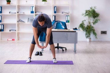 Genç yakışıklı çalışan ofiste spor egzersizleri yapıyor.