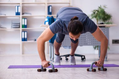 Genç yakışıklı çalışan ofiste spor egzersizleri yapıyor.