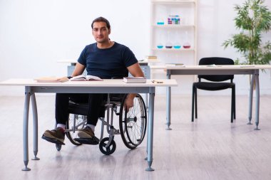 Tekerlekli sandalyedeki genç erkek öğrenci sınavlara hazırlanıyor.