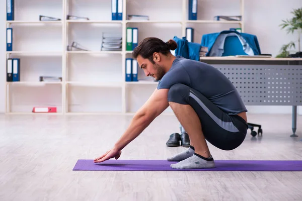 Jovem e bonito funcionário fazendo exercícios esportivos no escritório — Fotografia de Stock