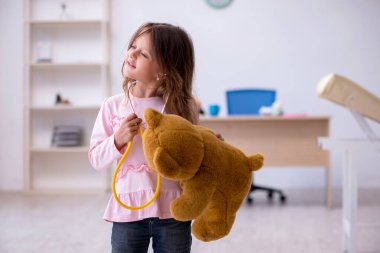 Küçük kız elinde oyuncak ayı klinikte doktoru bekliyor.
