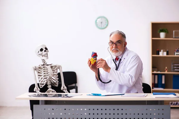 診療所での古い男性医師の心臓専門医と骨格患者 — ストック写真