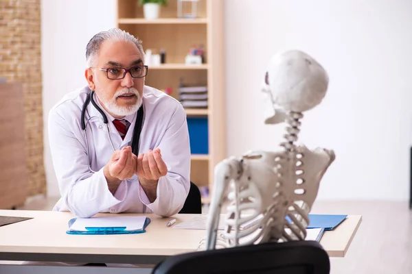 Oude mannelijke dokter en skelet patiënt in de kliniek — Stockfoto