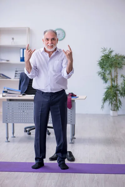 Verouderde mannelijke werknemer doet fysieke oefeningen tijdens de pauze — Stockfoto