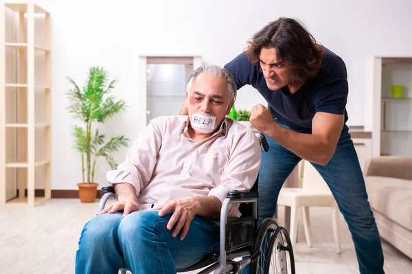 Oude man in rolstoel en jonge slechte verzorger binnen — Stockfoto