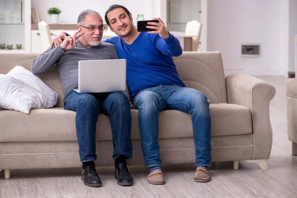 Ojciec i syn siedzą na kanapie z komputerem — Zdjęcie stockowe