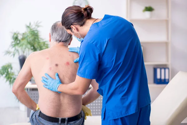 Homem velho visitando jovem médico dermatologista masculino — Fotografia de Stock