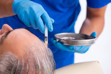 Yaşlı adam saç nakli için genç erkek doktoru ziyaret ediyor.