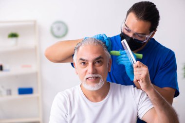 Yaşlı adam saç nakli için genç erkek doktoru ziyaret ediyor.