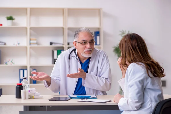 Yaşlı erkek doktor ve klinikteki genç bayan asistanı. — Stok fotoğraf