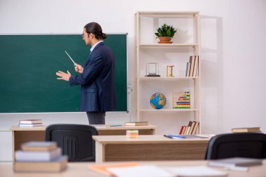 Genç erkek öğretmen yeşil panonun önünde.