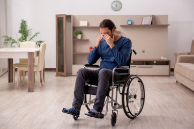 Evde acı çeken tekerlekli sandalyedeki genç adam.