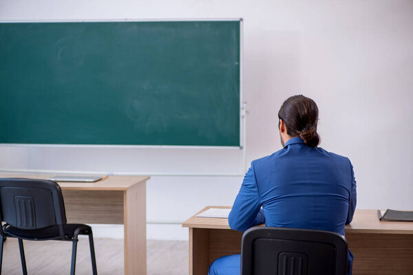 Young male teacher in suit in front of green board