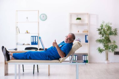 Yaşlı erkek doktor klinikte not alıyor.