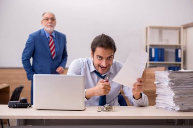 Genç erkek çalışan ve yaşlı patron iş yerinde kağıtları yakıyor.