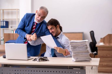 Genç erkek çalışan ve yaşlı patron iş yerinde kağıtları yakıyor.