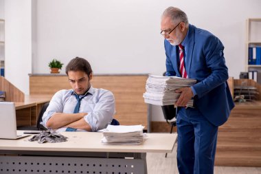Genç erkek çalışan ve yaşlı patron iş yerinde kağıtları yakıyor.