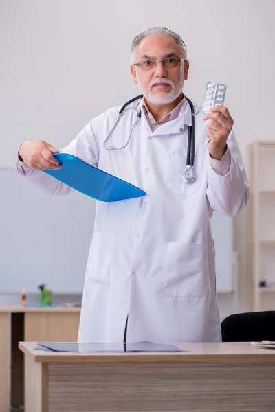 Stary lekarz sugerujący pigułki w klinice — Zdjęcie stockowe