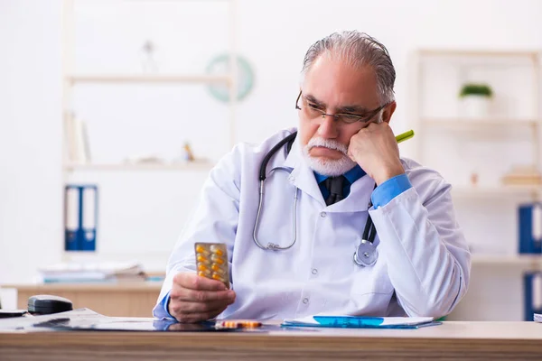 Old male doctor writing prescription in the clinic — Stock Photo, Image