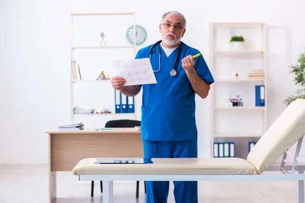 Old male doctor cardiologist looking electrocardiogram — Stock Photo, Image